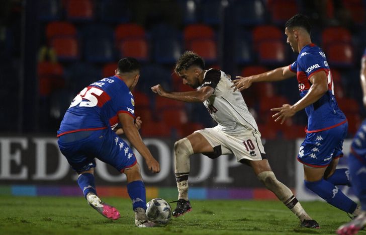 Marcelino Moreno, figura de Lanús, pasa entre dos rivales.