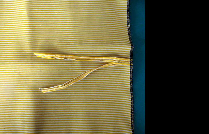 3. Realizar una tira con tela doble de 40 cm de largo. Superponer el revés de los rectángulos de tela (estampada y vinílica) y unirlos por todo el contorno con overlock o puntada zigzag tupida, integrando en la costura del lateral derecho la tira para atar doblada en dos.